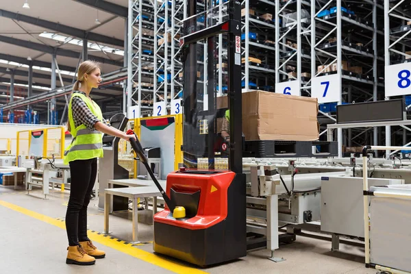 Storehouse medewerker in uniform werken aan vorkheftruck in moderne automatische warehouse.Boxen zijn op de planken van het magazijn. Opslag, machineconcept. Logistiek in stock. — Stockfoto