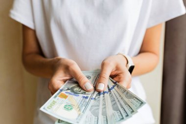 İş kadını nakit para almış. Zenginlik ve refah kavramı. Kadın elleri 100 dolarlık banknotları tutuyor. Beyaz gömlekli kadın, bej arka planda yığınla para tutuyor. Kolay nakit krediler.