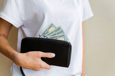 Cüzdanı kadının elinde. Nakit ödeme ya da alışveriş konsepti. Kız, siyah deri çantadan 100 doları bir çantada tutan parayı çıkardı. Finansal, bankacılık, alışveriş