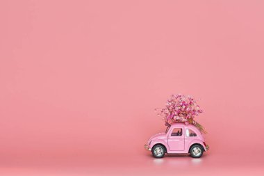 Pembe retro oyuncak araba pembe arka planda bir buket çiçek getiriyor. Sevgililer Günü, 14 Şubat kartı. Uluslararası Kadınlar Günü 8 Mart, Anneler Günü, Doğum günü hediyesi. Boşluğu kopyala, düzenle, şablonu en aza indir