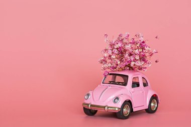 Pembe retro oyuncak araba pembe arka planda bir buket çiçek getiriyor. Sevgililer Günü, 14 Şubat kartı. Uluslararası Kadınlar Günü 8 Mart, Anneler Günü, Doğum günü hediyesi. Boşluğu kopyala, düzenle, şablonu en aza indir