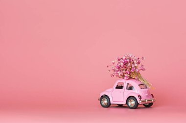 Pembe retro oyuncak araba pembe arka planda bir buket çiçek getiriyor. Sevgililer Günü, 14 Şubat kartı. Uluslararası Kadınlar Günü 8 Mart, Anneler Günü, Doğum günü hediyesi. Boşluğu kopyala, düzenle, şablonu en aza indir