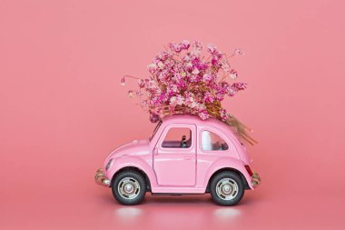 Pembe retro oyuncak araba pembe arka planda bir buket çiçek getiriyor. Sevgililer Günü, 14 Şubat kartı. Uluslararası Kadınlar Günü 8 Mart, Anneler Günü, Doğum günü hediyesi. Boşluğu kopyala, düzenle, şablonu en aza indir
