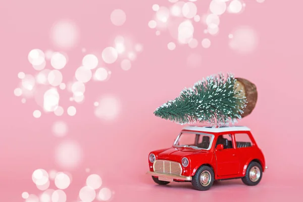 Red toy car with a christmas tree on the roof on pink paper background. Winter delivery, xmas, happy new year 2020 celebration concept. greeting card, mockup, copy space, place for text, template — Stock Photo, Image