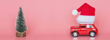 Changxing, Çin - 15 Ekim 2019 Noel Baba şapkalı kırmızı oyuncak araba, gelecek yılbaşı ağacı pembe kağıt arka planda. Kış teslimatı, xmas, mutlu yıllar 2020 kutlama konsepti. Tebrik kartı, maket, 