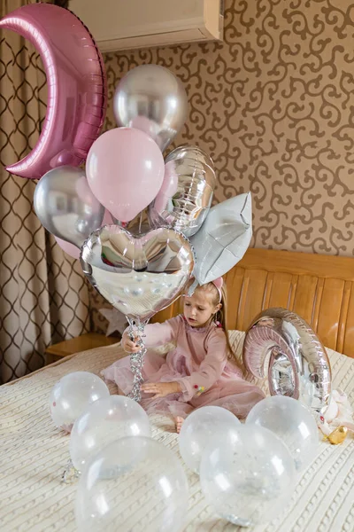 Vnitřní záběr pěkné radostné holčičky s blond vlasy slaví 6 let staré narozeniny s balónky, nosit módní šaty, mají vzrušené výrazy. Veselé vzpomínky z dětství — Stock fotografie