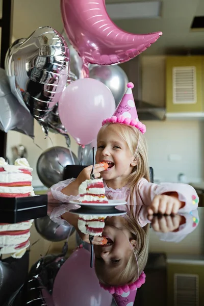 Indoor shot de niña bastante alegre con el pelo rubio soplando la vela, celebrar 6 años de edad cumpleaños, usar vestido de moda, tienen expresiones emocionadas. Concepto de infancia feliz —  Fotos de Stock