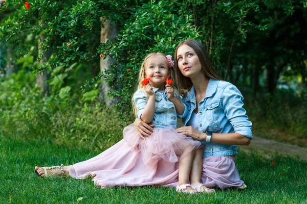 Portrait of beautiful woman and girl outdoor. Little daughter with her lovely mother in the summer park with blooming flowers. Happy mother\'s day concept. High quality photo
