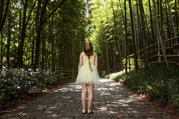 Jolie petite fille en robe de tutu jaune debout dans la forêt de bambous en Chine. Enfant avec des cheveux blonds par derrière extérieur — Photo