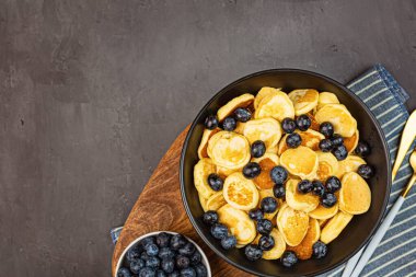 Gri beton arka planda küçük krepler ve yaban mersinli moda ev kahvaltısı. Düz konum, üst görünüm, genel görünüm, model, şablon, kopyalama alanı. Yukarıdan görüntüle