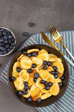 Gri beton arka planda küçük krepler ve yaban mersinli moda ev kahvaltısı. Düz konum, üst görünüm, genel görünüm, model, şablon, kopyalama alanı. Yukarıdan görüntüle