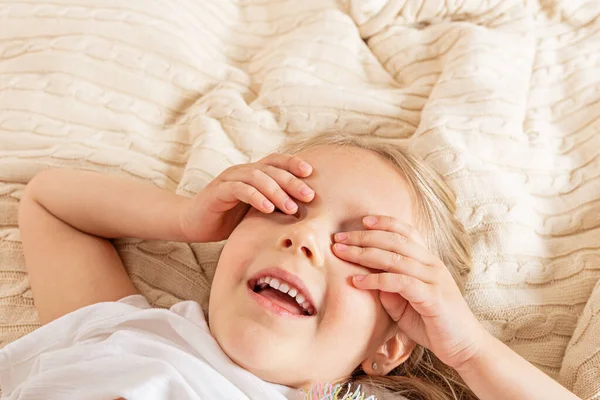 Красивая маленькая девочка в пижаме лежит на кровати дома. Оставайтесь дома во время коронавируса covid-19 и веселитесь. Концепция счастливого детства — стоковое фото