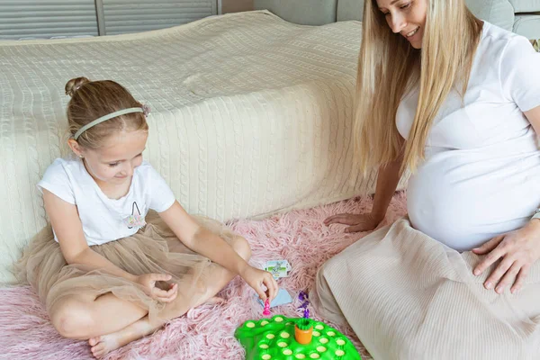 Prachtige blanke zwangere moeder en dochtertje die in de slaapkamer spelen. Blijf thuis tijdens de coronavirus covid-10 quarantaine. Familie plezier concept. — Stockfoto