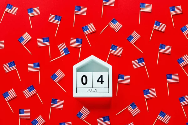 4 de julio. Burla de julio 4 calendario de color de madera y banderas de EE.UU. sobre fondo rojo. Día de la Independencia de América. Plano laico, vista superior, plantilla — Foto de Stock