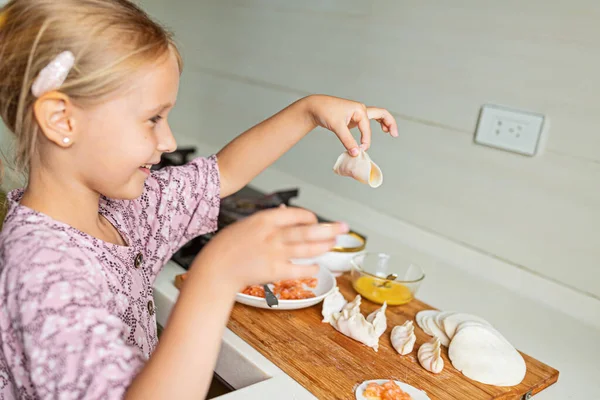 Jolie petite fille aux cheveux blonds cuisiner des boulettes avec du saumon cru sur la cuisine. Restez à la maison pendant la pandémie de coronavirus covid-19, concept de mode de vie sain. — Photo