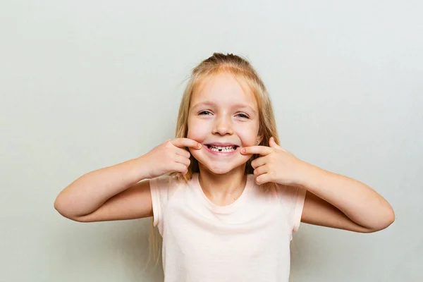 Парень показывает первый молочный зуб. Изменение концепции зубов. Милая маленькая девочка с светлыми волосами на сером фоне с копировальным пространством. — стоковое фото