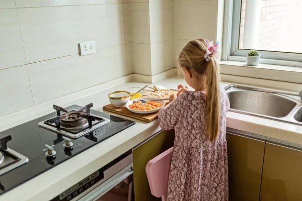 Cute little girl with blonde hair cooking dumplings with raw salmon on the kitchen. Stay at home during coronavirus covid-19 pandemic, healthy lifestyle concept.