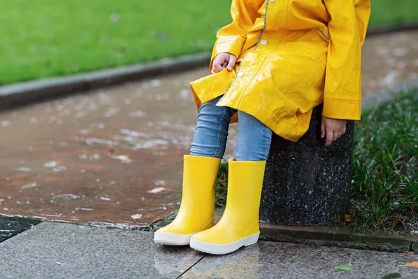 Cute little girl in yellow raincoat and rubber boots walking outdoor during rain. Bad weather, summer tropical storm, autumn fashion concept. High quality photo