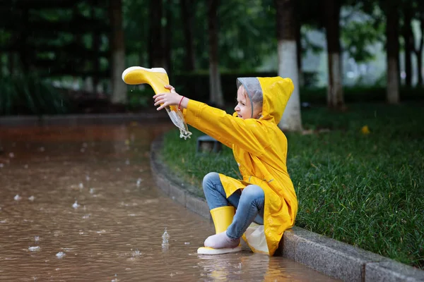 Carina bambina in impermeabile giallo e stivali di gomma che cammina all'aperto durante la pioggia. Maltempo, tempesta tropicale estiva, concetto di moda autunnale. — Foto Stock