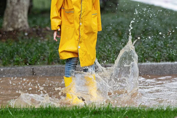 Carina bambina in impermeabile giallo e stivali di gomma che cammina all'aperto durante la pioggia. Maltempo, tempesta tropicale estiva, concetto di moda autunnale. — Foto Stock