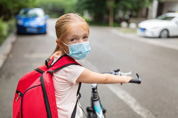 School child wearing face mask during coronavirus pandemic outbreak. Blonde girl going back to school after covid-19 quarantine and lockdown. Kid in medical mask for coronavirus prevention. New normal