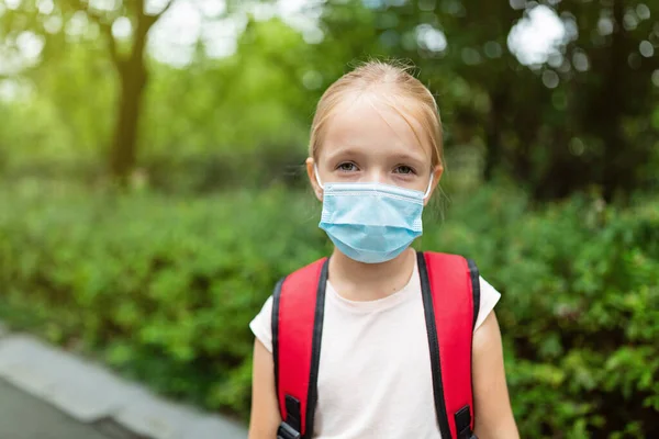 Uczennica nosząca maskę podczas epidemii koronawirusa. Blondynka wraca do szkoły po kwarantannie i zamknięciu. Dzieciak w masce medycznej do zapobiegania koronawirusom. Nowa normalna — Zdjęcie stockowe