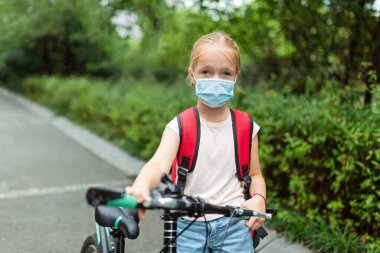 Koronavirüs salgını sırasında yüz maskesi takan okul çocuğu. Sarışın kız, karantina ve tecritten sonra okula geri dönüyor. Coronavirus önleme için tıbbi maskeli bir çocuk. Yeni normal