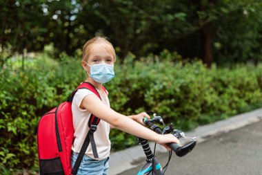 Koronavirüs salgını sırasında yüz maskesi takan okul çocuğu. Sarışın kız, karantina ve tecritten sonra okula geri dönüyor. Coronavirus önleme için tıbbi maskeli bir çocuk. Yeni normal