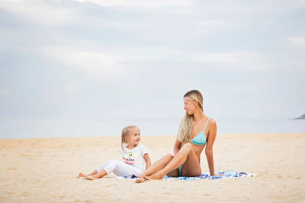 Beautiful sexy young caucasian woman in blue bikini and little girl on the sandy beach. Summer family vacations, travel and tourism concept after end of coronavirus covid-19 lockdown. Copy space. High quality photo