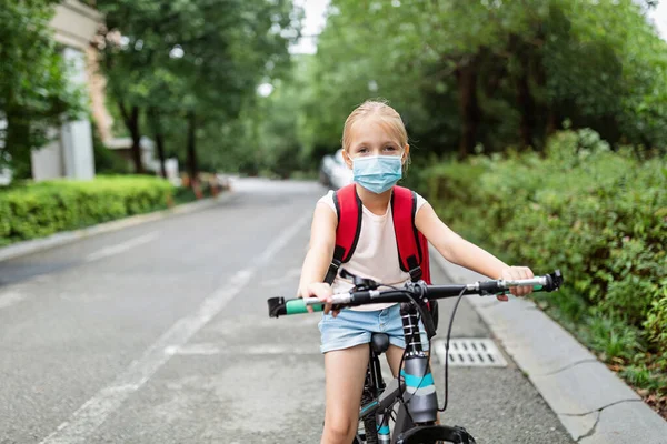 School child wearing face mask during coronavirus pandemic outbreak. Blonde girl going back to school after covid-19 quarantine and lockdown. Kid in medical mask for coronavirus prevention. New normal. High quality photo