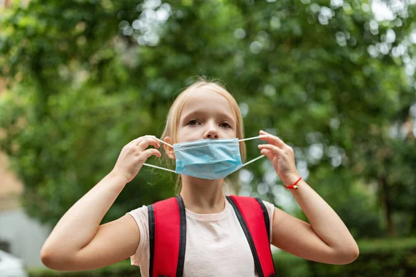 School child after end coronavirus pandemic outbreak. Blonde girl going back to school after covid-19 quarantine and lockdown. Happy kid outdoor. New normal. High quality photo