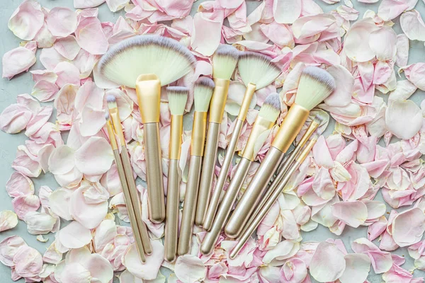 Cosmetic Makeup brushes on pink rose petals. Flat lay, top view, copy space. Makeup accessories, mockup, template.