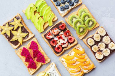 Krem peynirli sandviç, çikolatalı taze meyve ve böğürtlen avokado, yabanmersini, muz, kivi, kiraz, kayısı, gri bir zeminde ejderha meyvesi. Üst Manzara. Düz yatıyordu. Sağlıklı beslenme. Yüksek kalite fotoğraf