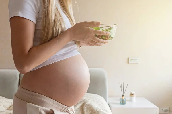 Glad ung gravid kvinna äter grönsakssallad hemma. Hälsosam kost och graviditet koncept. Förväntad moderskål med färska gurkor och tomater — Stockfoto