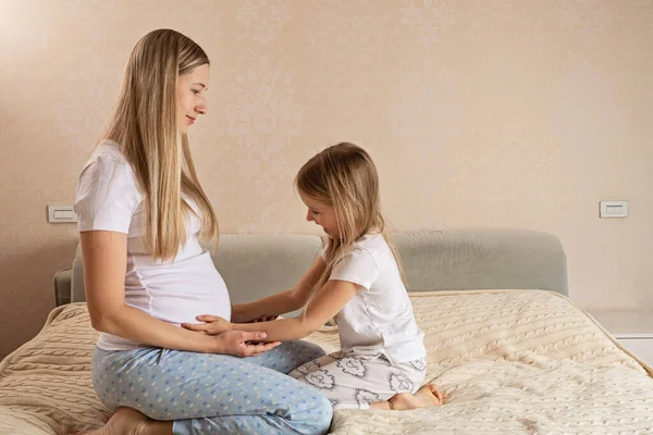 Felice figlia caucasica toccando la sua pancia madre incinta, seduta sul divano a casa durante l'isolamento coronavirus covid-19 quarantena, spazio vuoto — Foto Stock