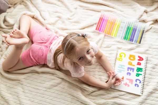 Little child english online at home. Homeschooling and distance education for kids. Girl student drawing english letters at the notebook during coronavirus covid-19 quarantine. High quality photo