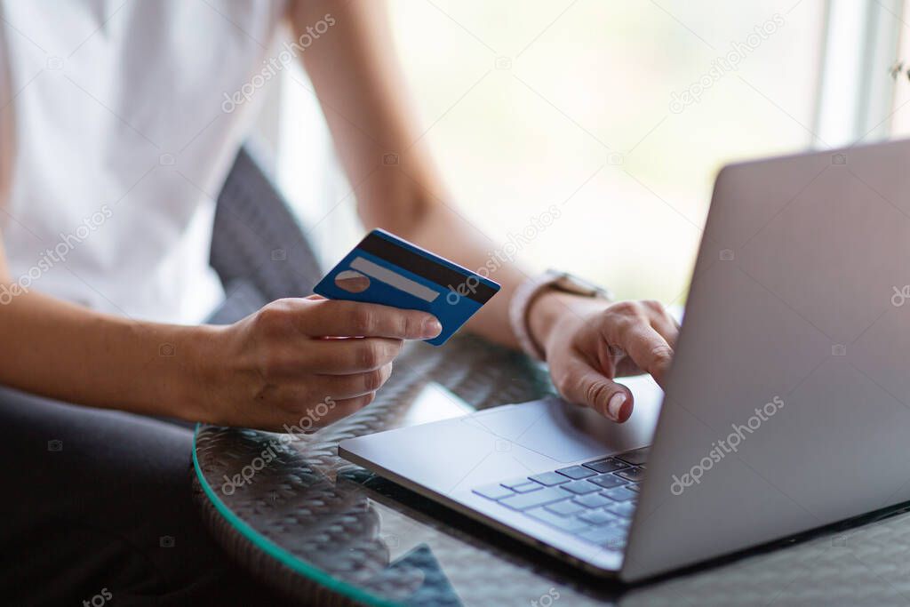 Young woman holding credit card and using laptop computer. Online shopping, e-commerce, internet banking, spending money, working from home concept. High quality photo