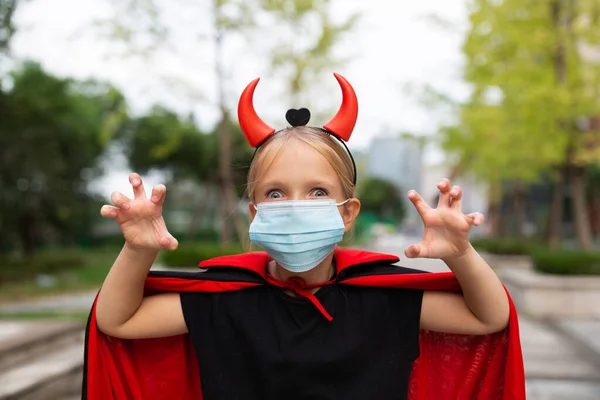 Portrait of cute Little Girl in costume of evil at home. Happy Halloween during coronavirus covid-19 pandemic quarantine concept. Kid wearing medical mask — Stock Photo, Image