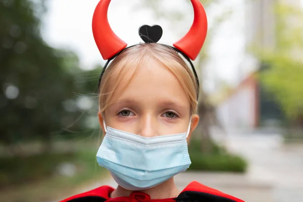 Portrait of cute Little Girl in costume of evil at home. Happy Halloween during coronavirus covid-19 pandemic quarantine concept. Kid wearing medical mask — Stock Photo, Image