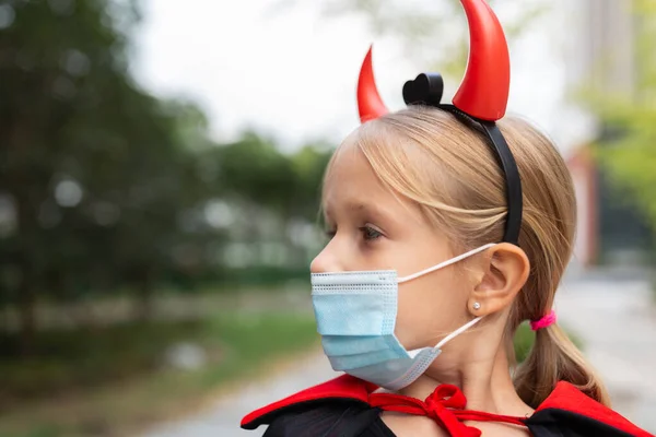 Portret uroczej dziewczynki w kostiumie zła w domu. Wesołego Halloween podczas kwarantanny coronavirus covid-19. Dzieciak w masce medycznej — Zdjęcie stockowe