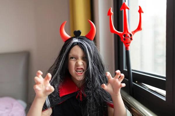 Little Girl in costume of devil with red horns at home. Happy Halloween concept. High quality photo