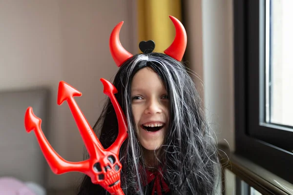 Little Girl in costume of devil with red horns at home. Happy Halloween concept. High quality photo