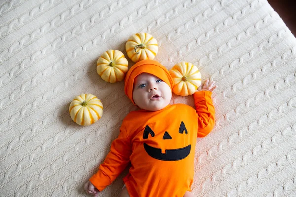 Вид с высоты угла на ребенка в костюме тыквы. Happy Kid 2 months old in orange Halloween costume on bed — стоковое фото