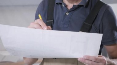 tulum ve mavi t-shirt uzman beyaz kağıt çizim bakar ve kalem yakın görünümü ile işaretleri yapar