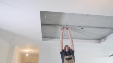 tulum ve gri t-shirt profesyonel handyman beyaz tavandan elektrik kabarcığı ile büyük tel alır