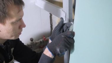 siyah eldiven yetenekli handyman borulara karşı metal maket bıçağı ile büyük alçıpan levha ve keser tutar