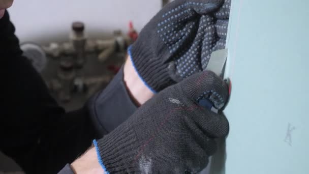 黒い綿の手袋でプロの修理工の手は 金属ボックスカッターの近いビューで青い石膏ボードをカット — ストック動画