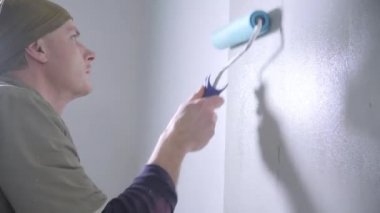 kahverengi tulum ve siyah pullover odaklanmış handyman dikkatle yakın görünümü beyaz duvarda mavi tutkal rulo çalışır