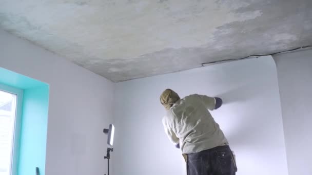 プロの便利な人は 窓付きの新しいフラットで電気光の下で壁に白い壁紙をハングアップ — ストック動画