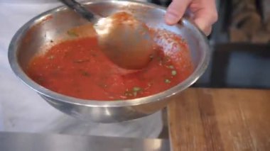 Pizzacı, sosu kasede baharatlarla karıştırıyor.